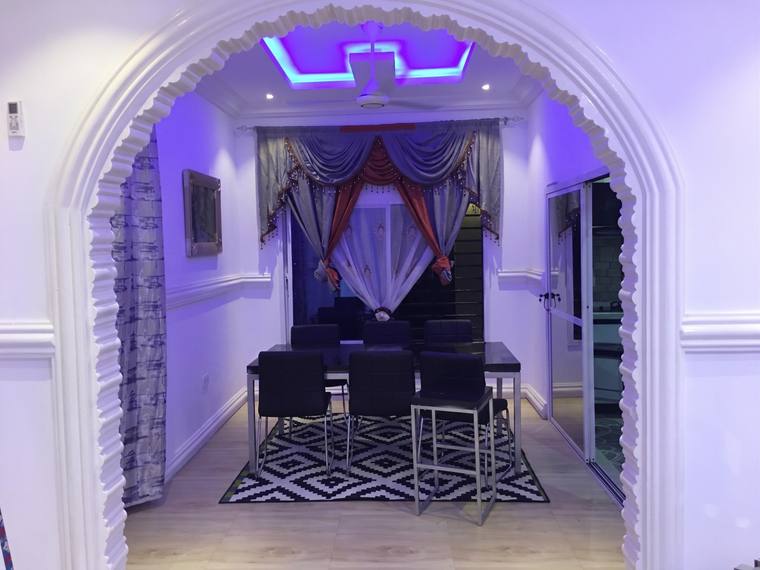 A dining table and six chairs seen through a moulded internal arch, with a curtained window bay behind and cove lighting to the ceiling.